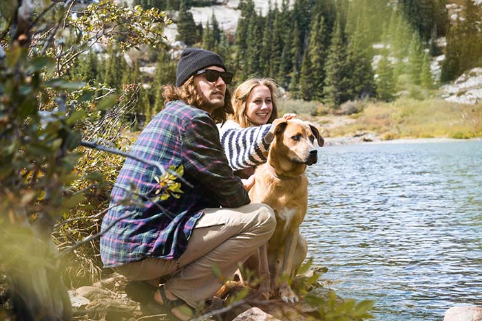 A boy and a girl sitting with dog near a river